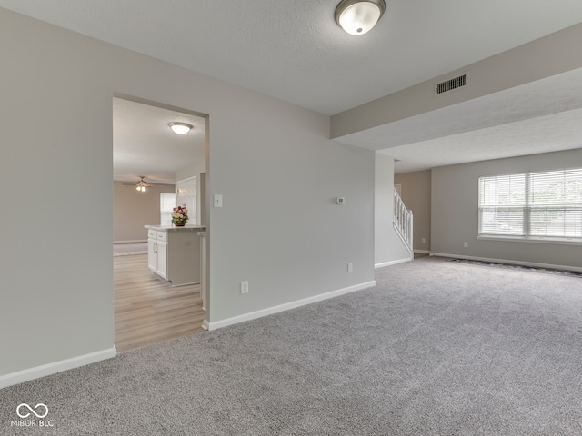 unfurnished room with baseboards, visible vents, light carpet, and stairway