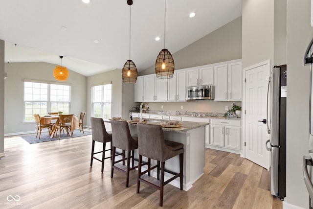 11595 Platt St, Noblesville, IN 46060 - kitchen featuring appliances with stainless steel finishes, white cabinets, high vaulted ceiling, light wood finished floors, and light stone countertops