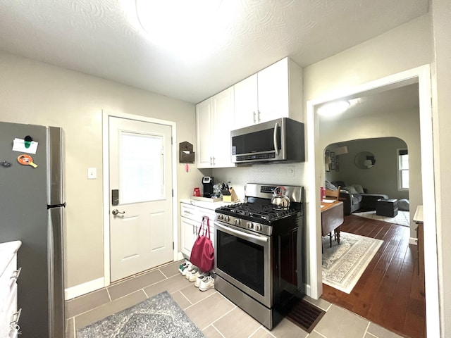 kitchen featuring light countertops, appliances with stainless steel finishes, arched walkways, and white cabinetry