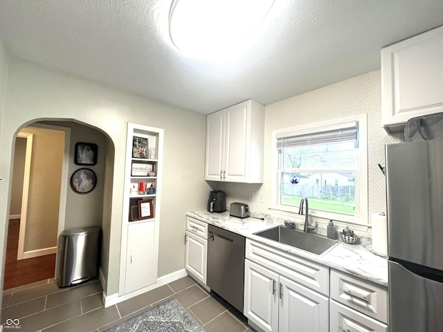 kitchen with dark tile patterned floors, arched walkways, white cabinets, a sink, and stainless steel appliances