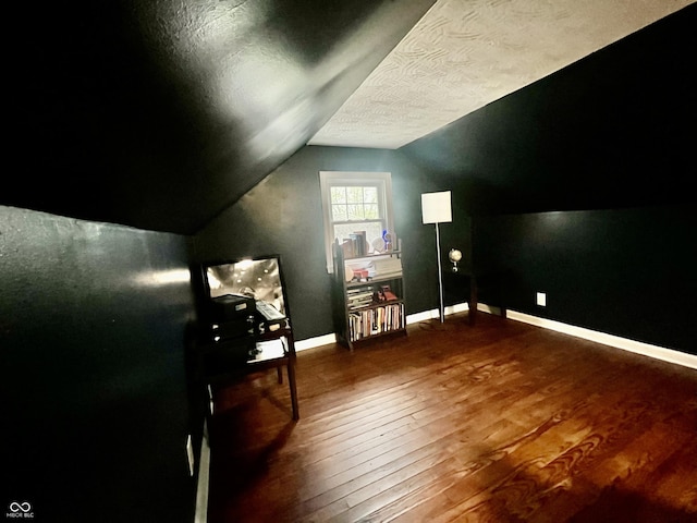 additional living space featuring baseboards, vaulted ceiling, hardwood / wood-style flooring, and a textured ceiling
