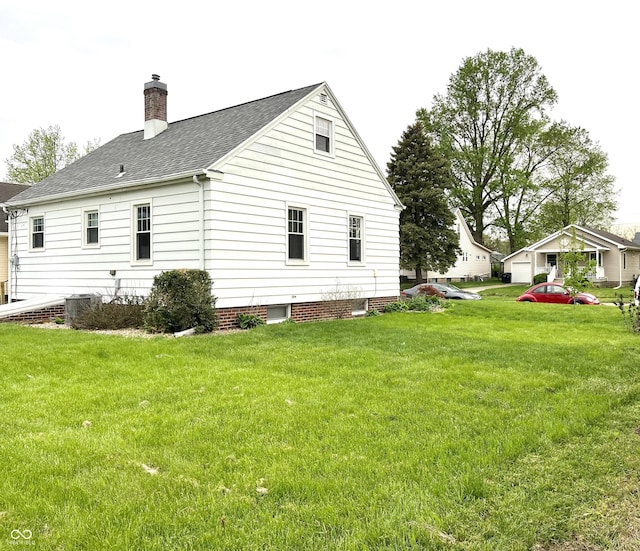 view of side of home with roof with shingles, a chimney, and a yard