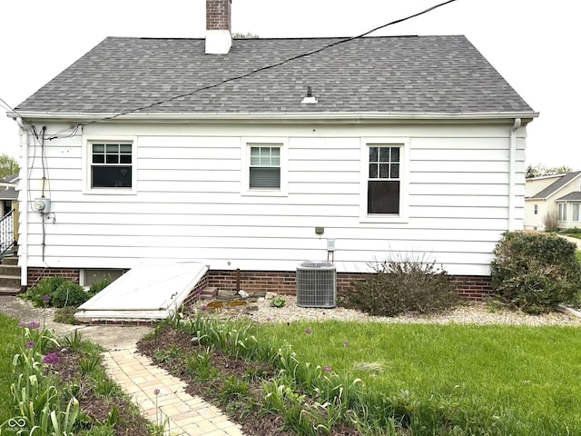back of house with central AC, a shingled roof, and a chimney