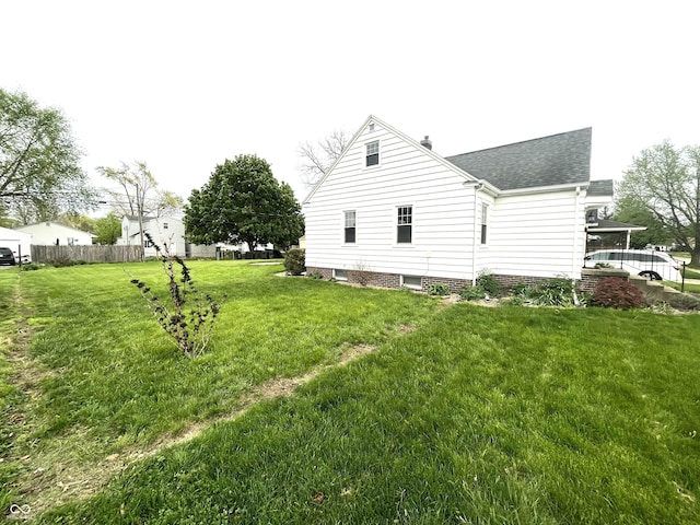 view of property exterior featuring a shingled roof, fence, and a yard