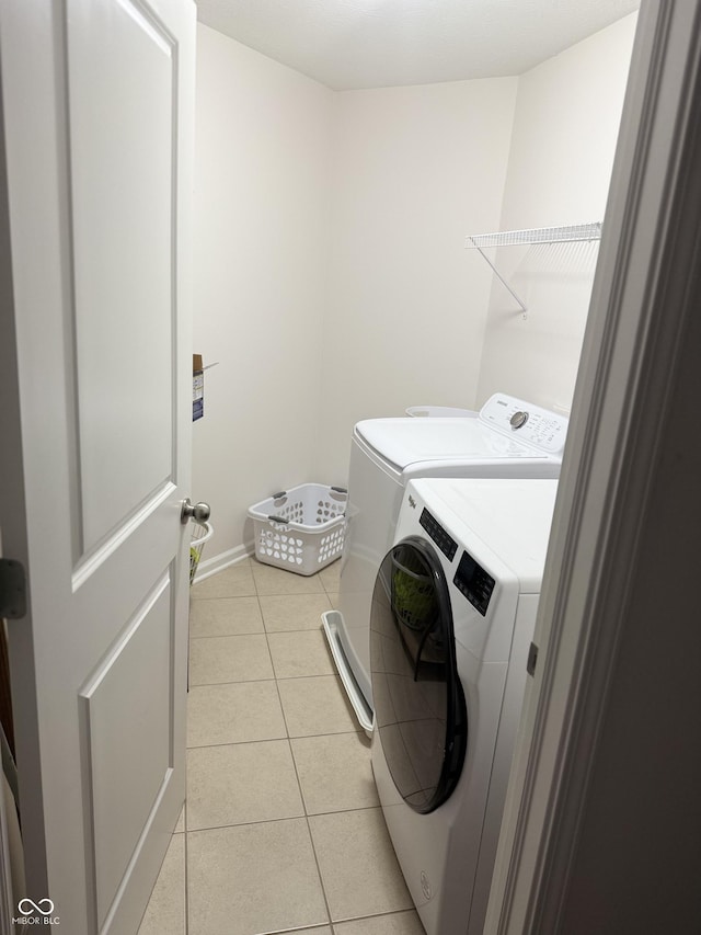 washroom with independent washer and dryer, light tile patterned flooring, laundry area, and baseboards