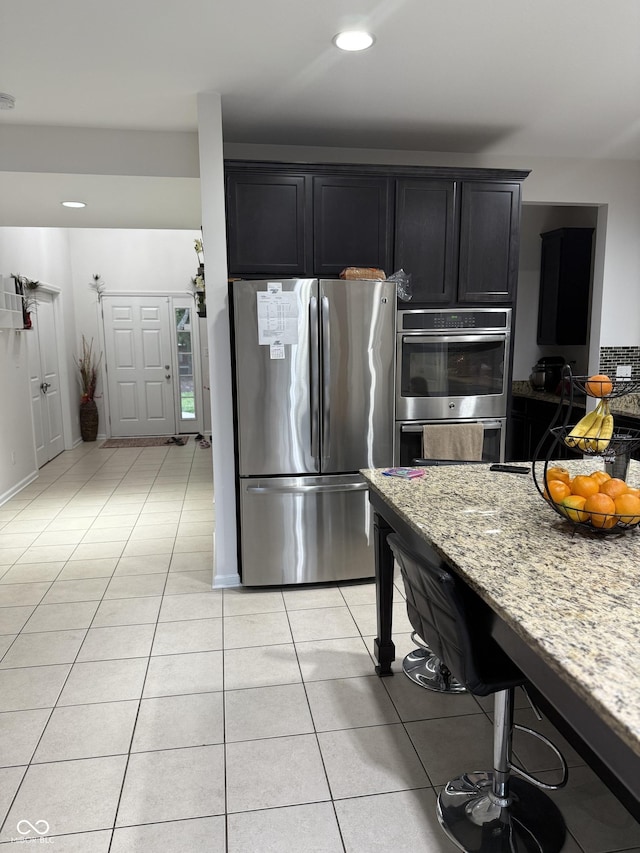 kitchen featuring light stone counters, dark cabinetry, light tile patterned floors, and stainless steel appliances