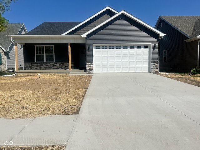 view of front of home featuring roof with shingles, stone siding, a garage, a porch, and driveway
