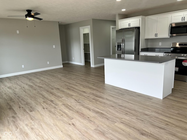kitchen with white cabinets, dark countertops, appliances with stainless steel finishes, ceiling fan, and a center island