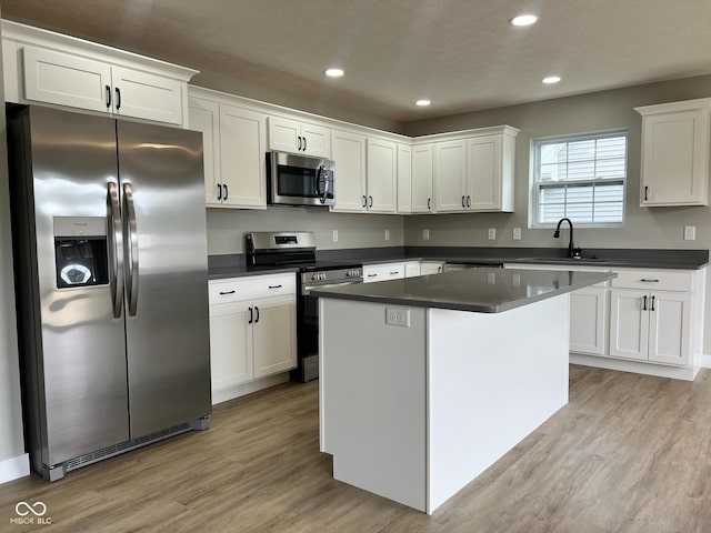 kitchen with light wood finished floors, appliances with stainless steel finishes, dark countertops, and white cabinetry