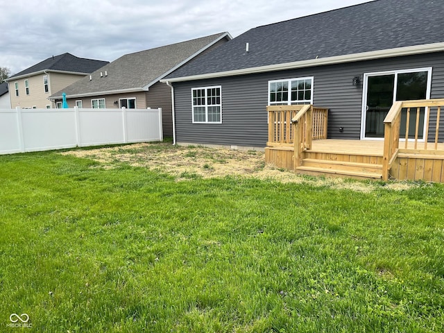 back of house with a shingled roof, a wooden deck, a yard, and fence