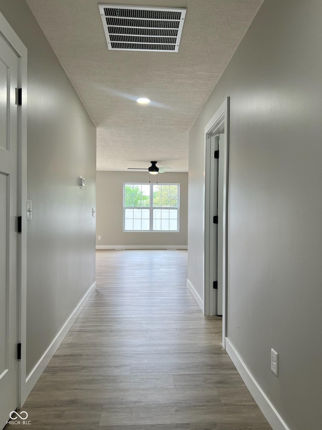 corridor with a textured ceiling, baseboards, visible vents, and wood finished floors