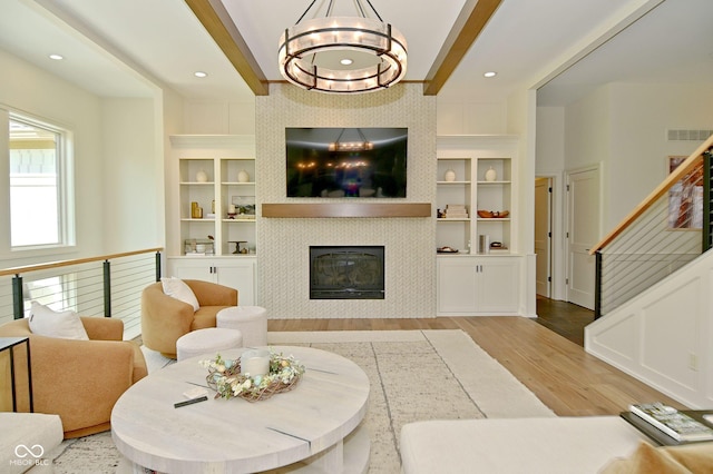 living area with wood finished floors, visible vents, built in shelves, a fireplace, and a notable chandelier