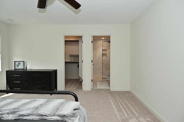 bedroom with carpet, ensuite bath, a spacious closet, a ceiling fan, and baseboards