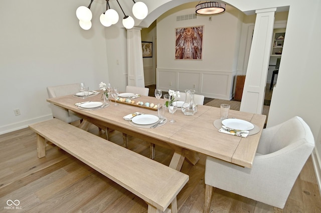 dining area featuring a decorative wall, a wainscoted wall, wood finished floors, ornate columns, and arched walkways