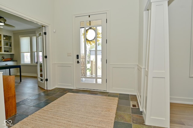 foyer entrance with a decorative wall, a wainscoted wall, and stone tile flooring