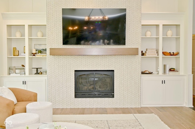 living area with built in features, light wood-style flooring, and a tile fireplace