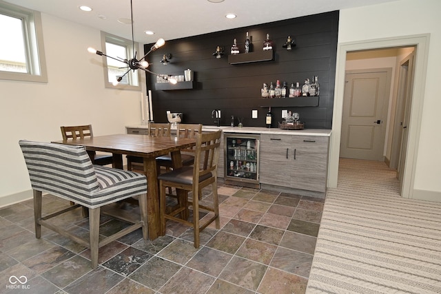bar featuring a dry bar, recessed lighting, an inviting chandelier, stone finish flooring, and beverage cooler
