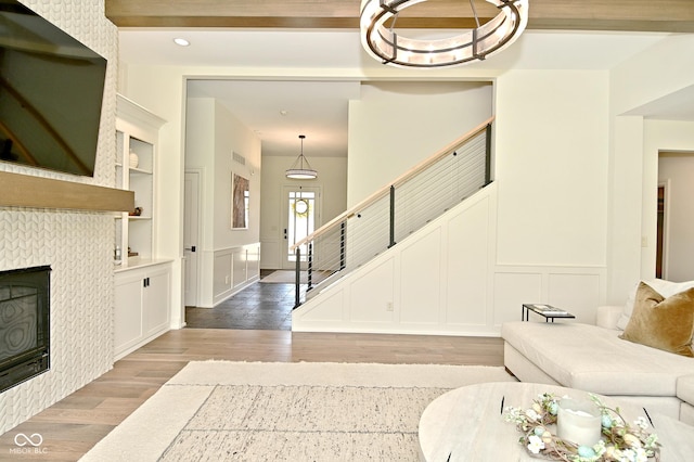 living room with a tiled fireplace, a decorative wall, light wood-type flooring, and built in features