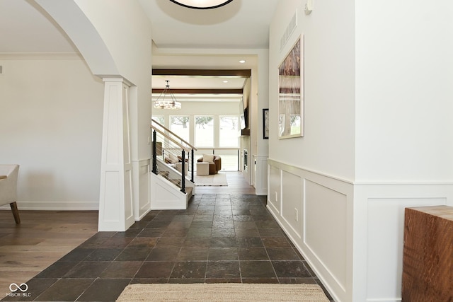 corridor featuring stairs, a decorative wall, stone tile flooring, visible vents, and arched walkways