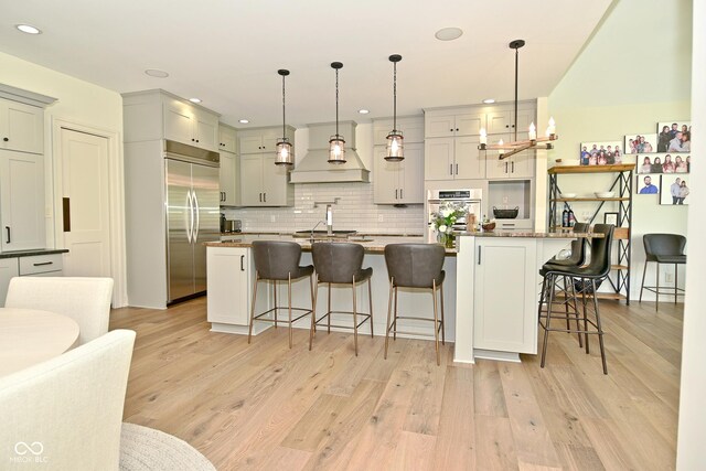 kitchen with premium range hood, stainless steel appliances, decorative backsplash, and light wood-style flooring