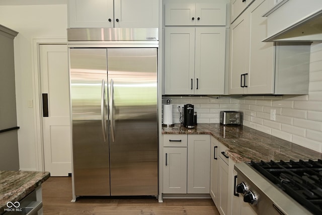 kitchen featuring dark stone counters, stainless steel appliances, extractor fan, dark wood-style flooring, and tasteful backsplash