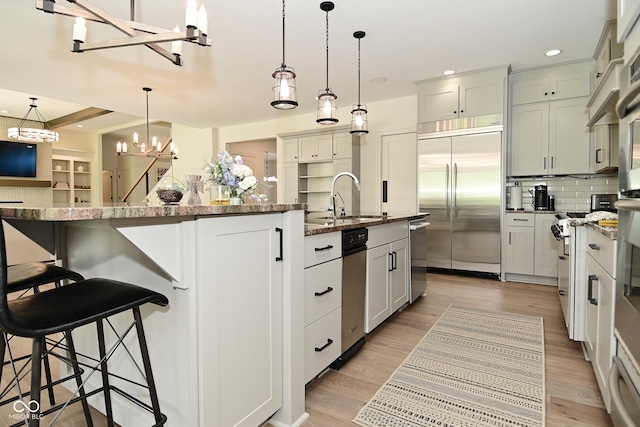 kitchen with a sink, stainless steel appliances, a kitchen island with sink, pendant lighting, and a chandelier