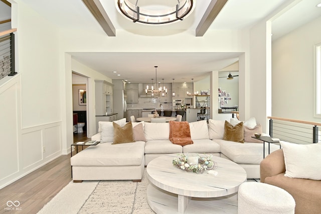 living area with a decorative wall, light wood-style flooring, beam ceiling, and a wainscoted wall