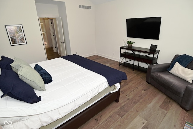 bedroom with baseboards, vaulted ceiling, visible vents, and wood finished floors