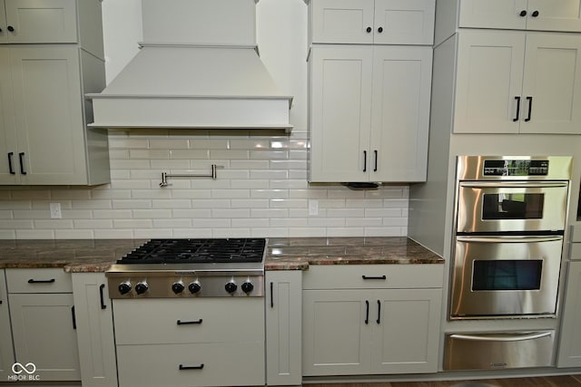 kitchen with dark stone countertops, backsplash, appliances with stainless steel finishes, a warming drawer, and custom exhaust hood