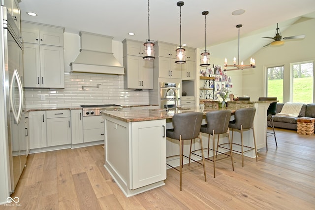 kitchen featuring premium range hood, stainless steel appliances, light wood-style flooring, decorative backsplash, and light stone countertops