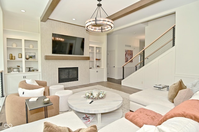 living area with stairs, wood finished floors, built in shelves, a fireplace, and a chandelier
