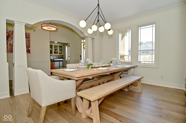 dining room featuring baseboards, crown molding, arched walkways, light wood-type flooring, and ornate columns