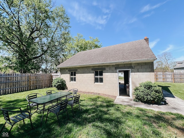rear view of house with a lawn, roof with shingles, a fenced backyard, and concrete block siding