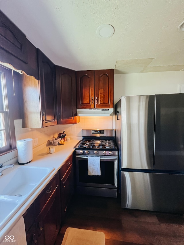 kitchen with dark wood finished floors, light countertops, a sink, under cabinet range hood, and stainless steel appliances