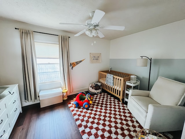 bedroom featuring a nursery area, ceiling fan, baseboards, and dark wood-type flooring