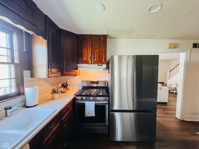 kitchen featuring a sink, light countertops, dark wood finished floors, stainless steel appliances, and under cabinet range hood