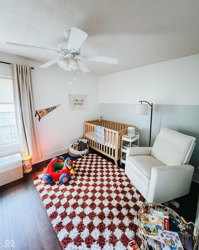 bedroom featuring a crib, ceiling fan, and wood finished floors