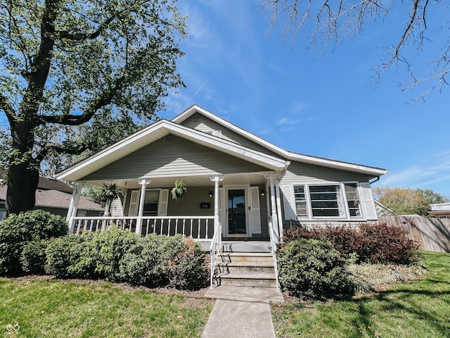 bungalow-style home featuring fence, a porch, and a front lawn