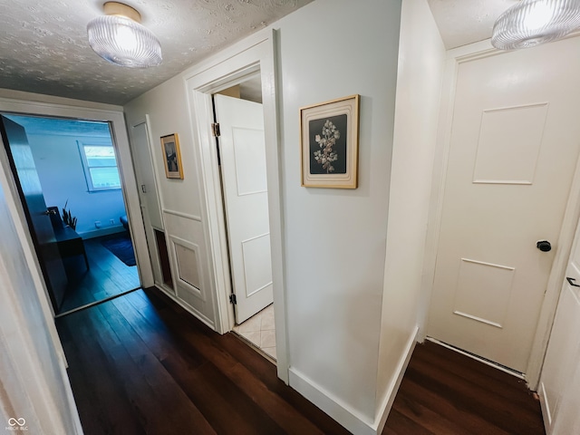 hallway with baseboards, a textured ceiling, and wood finished floors