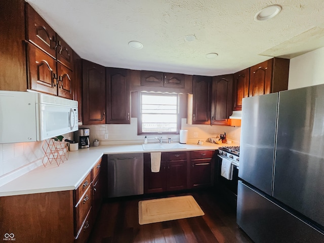 kitchen featuring appliances with stainless steel finishes, a sink, light countertops, tasteful backsplash, and dark wood-style floors