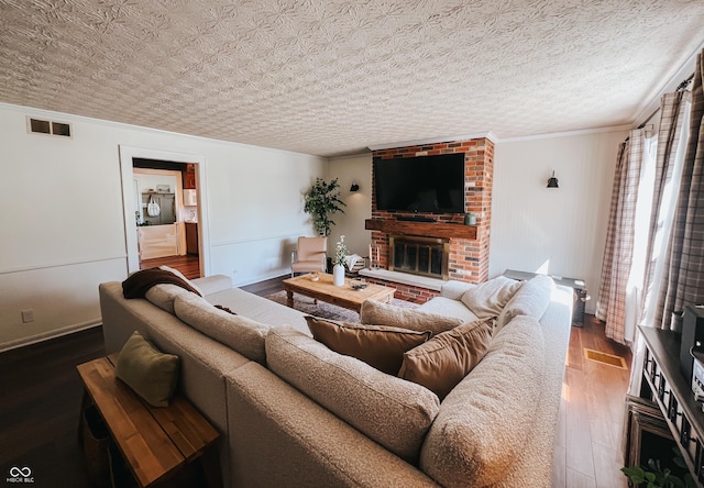 living area with visible vents, crown molding, a brick fireplace, wood finished floors, and baseboards