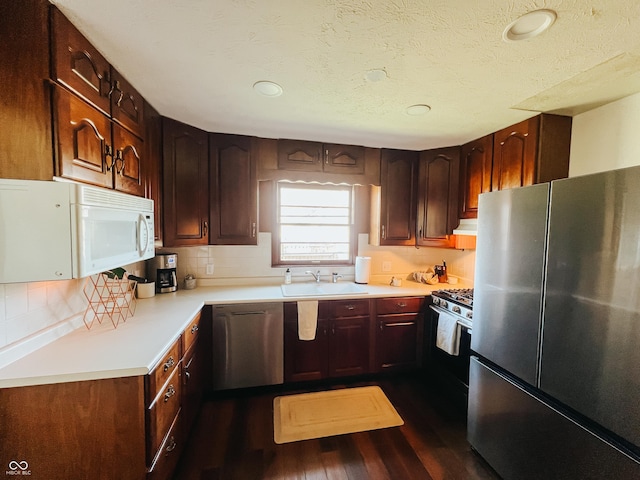 kitchen featuring dark wood-style flooring, light countertops, a sink, backsplash, and stainless steel appliances