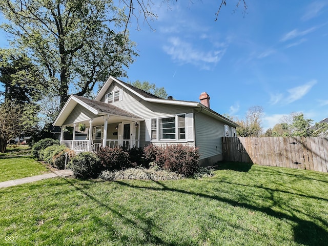 bungalow-style house featuring a porch, a front lawn, fence, and a chimney
