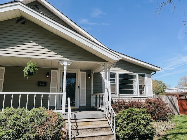 view of exterior entry with a porch and fence