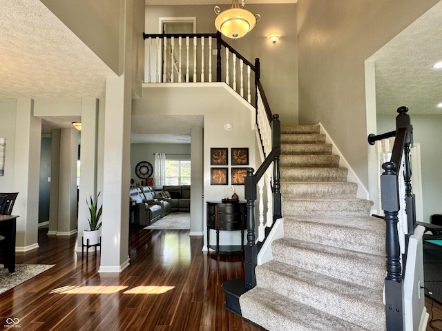 stairs featuring a textured ceiling, baseboards, wood finished floors, and a towering ceiling