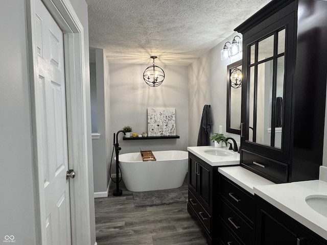 full bathroom with a sink, a textured ceiling, two vanities, wood finished floors, and a soaking tub