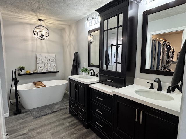 bathroom with a soaking tub, a textured ceiling, a sink, and wood finished floors