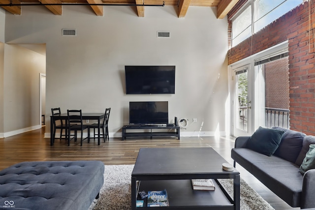 living area with beamed ceiling, wood finished floors, a towering ceiling, and baseboards