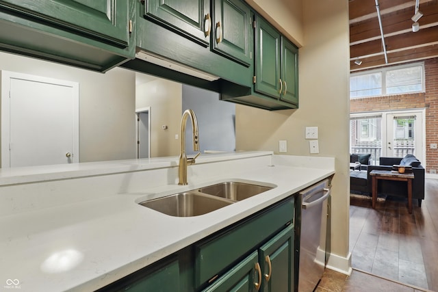 kitchen featuring green cabinets, a sink, stainless steel dishwasher, light countertops, and brick wall