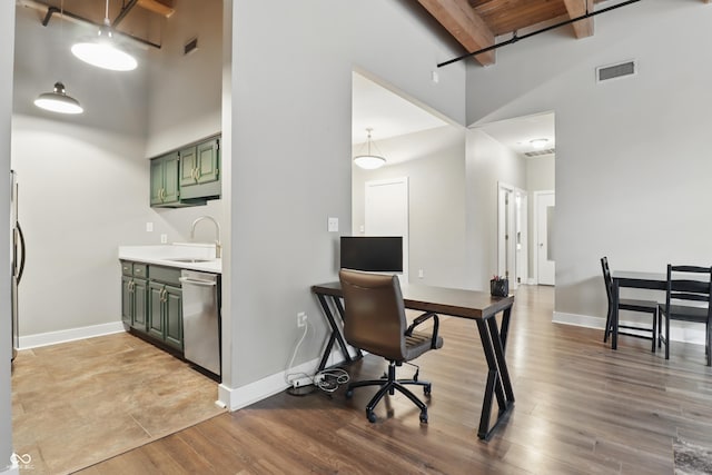 home office with a towering ceiling, a sink, beam ceiling, light wood-type flooring, and baseboards